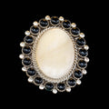 Ring with a large oval of mother of pearl and smaller onyx stones around on a black background
