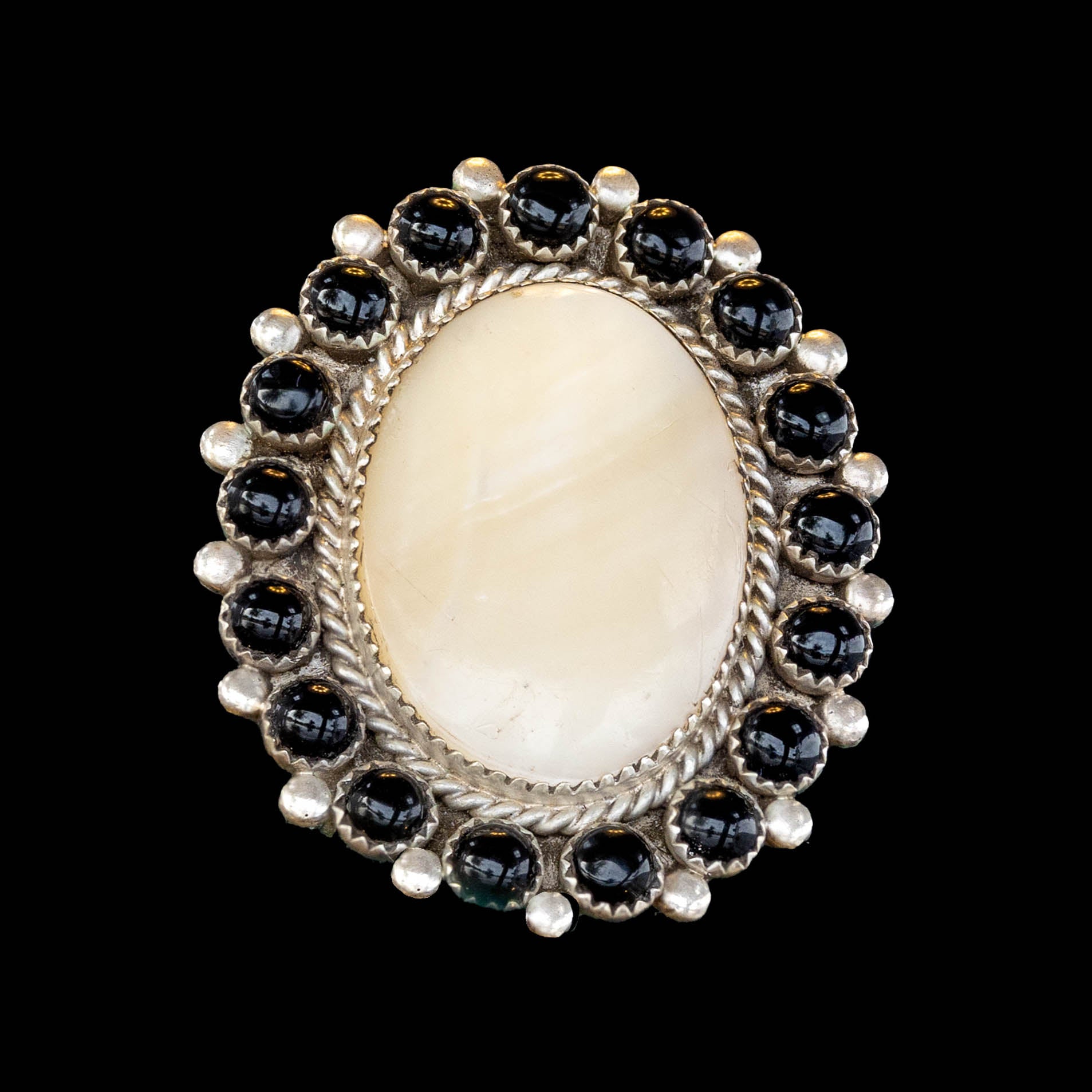 Ring with a large oval of mother of pearl and smaller onyx stones around on a black background