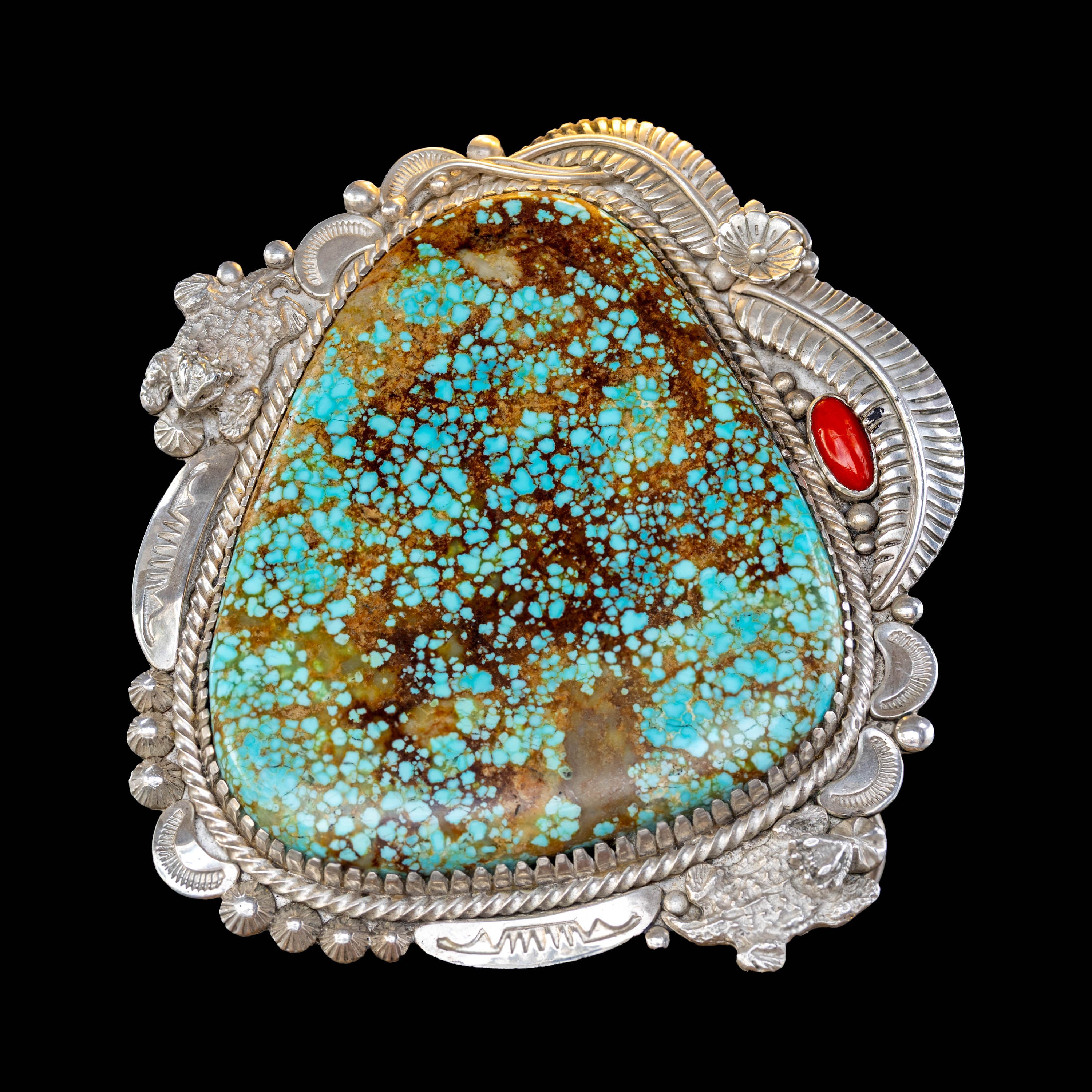 Large turquoise stone with silver border on a black background with silver castings