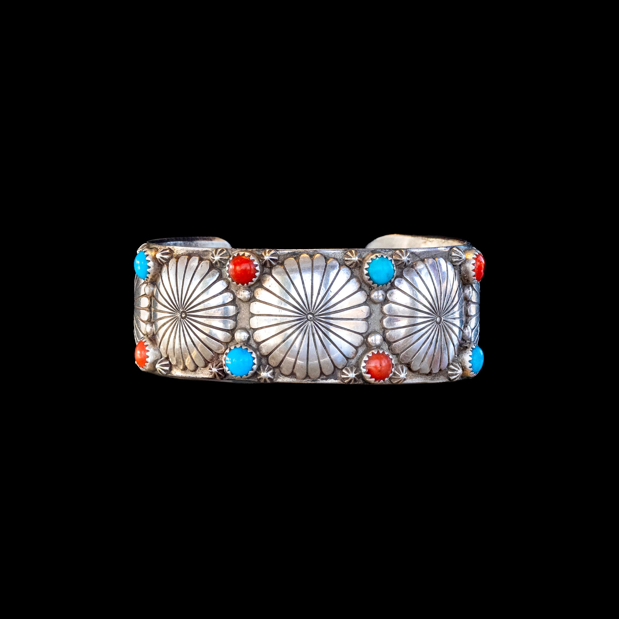 Silver bracelet with sunburst designs and colorful stones on a black background