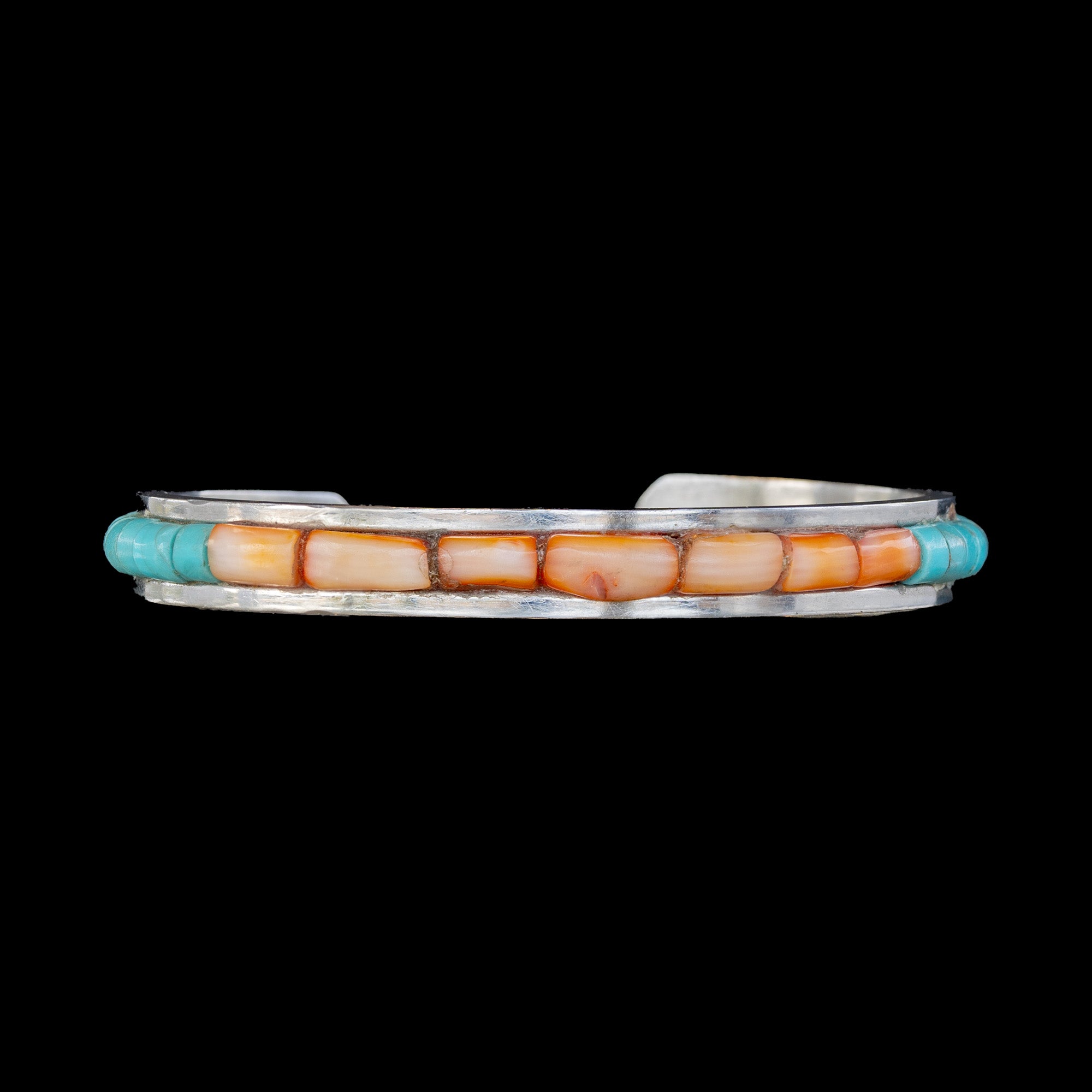Cuff bracelet with turquoise and coral set in silver channel on a black background